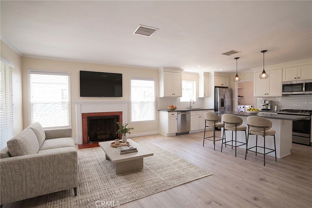 Open great room with white kitchen, fireplace, oak-tone flooring, and counter-height pendant lighting